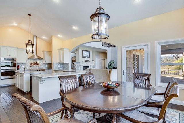 dining space featuring dark wood-type flooring, sink, high vaulted ceiling, and a notable chandelier