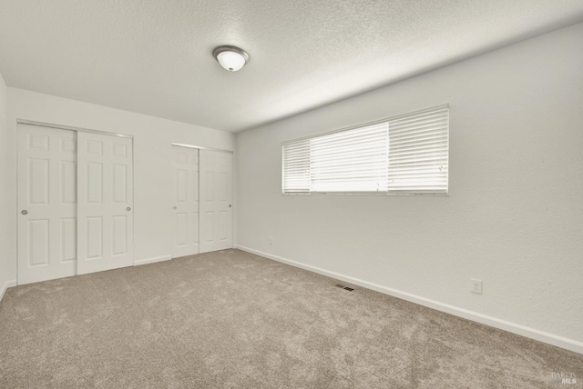 unfurnished bedroom featuring multiple closets, a textured ceiling, and carpet flooring