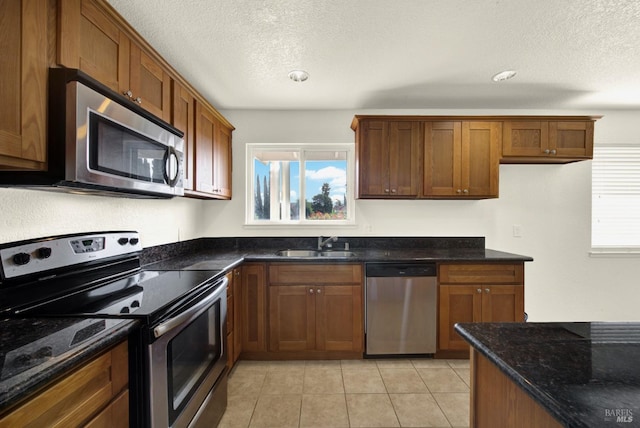 kitchen featuring sink, dark stone counters, light tile patterned floors, stainless steel appliances, and a textured ceiling