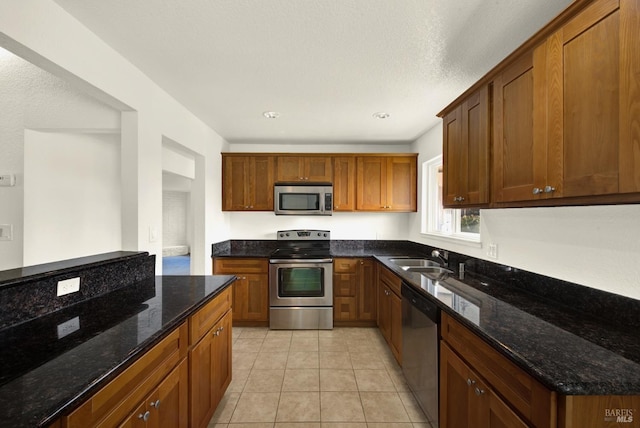 kitchen with appliances with stainless steel finishes, sink, light tile patterned floors, and dark stone counters