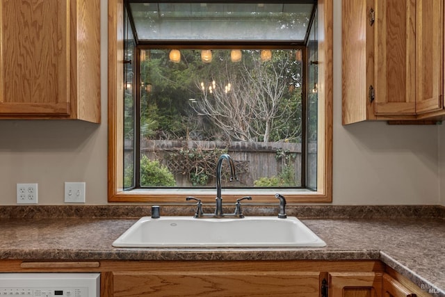 kitchen featuring brown cabinetry, dark countertops, a sink, and dishwasher