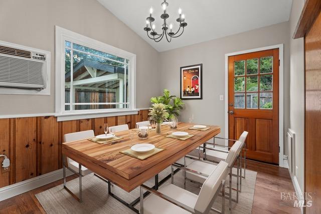 dining area featuring an inviting chandelier, lofted ceiling, a wall mounted AC, and wood-type flooring