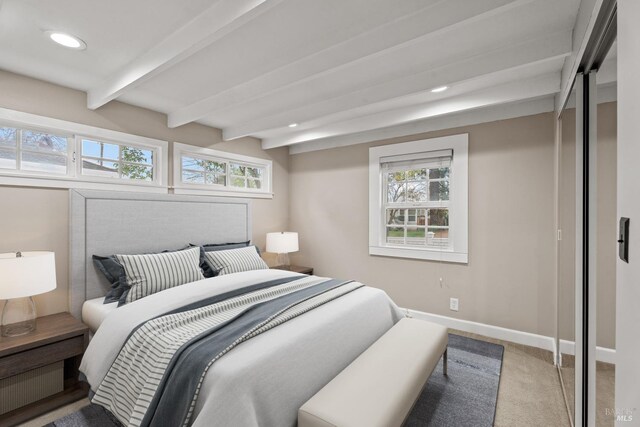 bedroom with beamed ceiling and light colored carpet