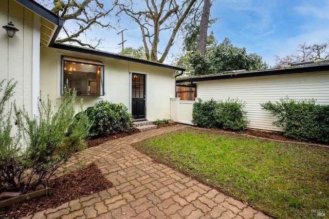 entrance to property featuring a lawn, a patio area, fence, and stucco siding