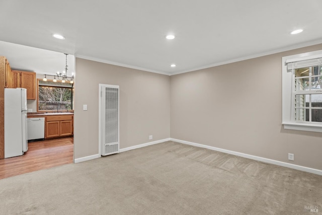 spare room featuring a chandelier, light carpet, ornamental molding, and baseboards