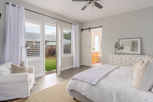 bedroom with connected bathroom, access to exterior, ceiling fan, a barn door, and light hardwood / wood-style floors