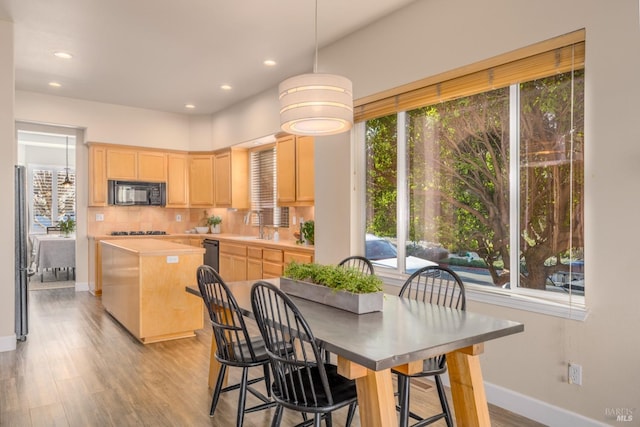 kitchen with light brown cabinetry, gas stovetop, light hardwood / wood-style flooring, stainless steel refrigerator, and backsplash