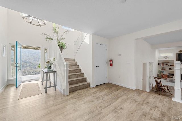 entrance foyer featuring stairs, baseboards, a chandelier, and light wood-style floors