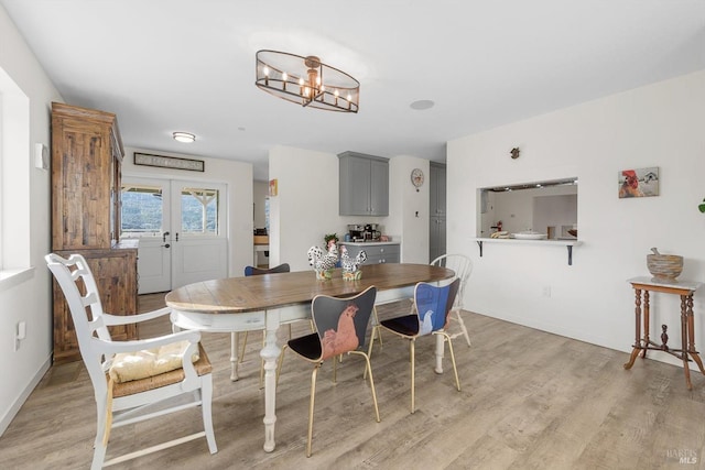 dining room featuring light wood-style floors, french doors, a notable chandelier, and baseboards