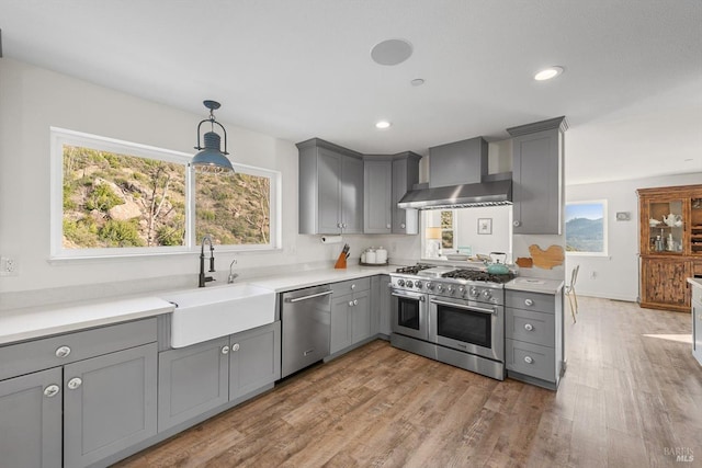 kitchen with appliances with stainless steel finishes, light countertops, a sink, and wall chimney exhaust hood