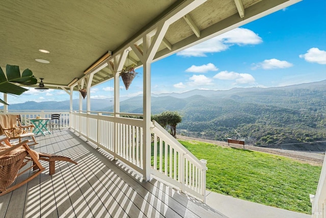 wooden terrace featuring ceiling fan, a lawn, and a mountain view