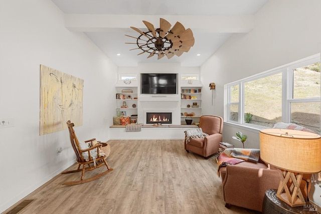 sitting room with a large fireplace, beamed ceiling, and wood finished floors