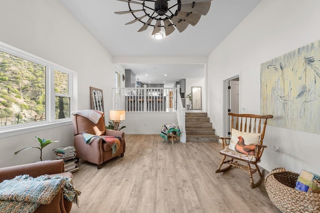 living area with a ceiling fan, baseboards, light wood finished floors, and stairs