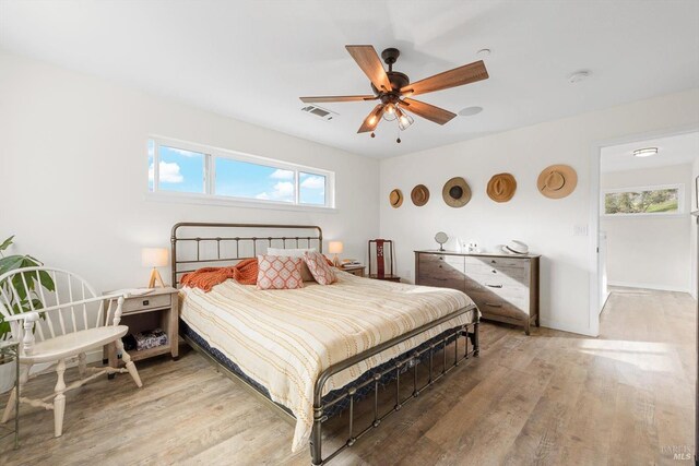 bedroom with a ceiling fan, wood finished floors, visible vents, and baseboards