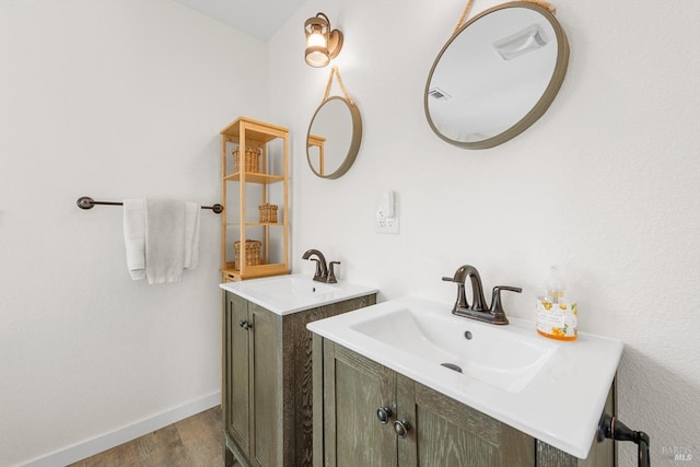 bathroom featuring wood finished floors, two vanities, a sink, and baseboards