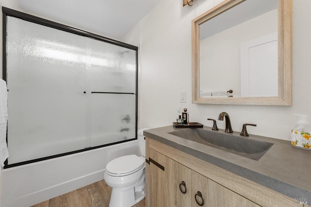 full bathroom featuring toilet, combined bath / shower with glass door, wood finished floors, and vanity