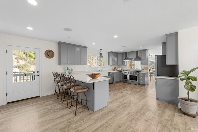 kitchen with appliances with stainless steel finishes, a peninsula, light countertops, gray cabinetry, and wall chimney range hood