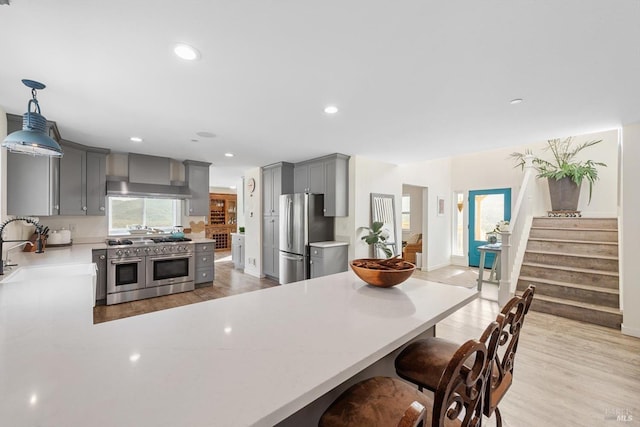 kitchen with wall chimney exhaust hood, appliances with stainless steel finishes, hanging light fixtures, gray cabinets, and light countertops