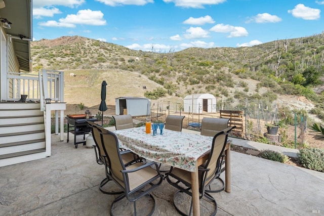 view of patio / terrace with outdoor dining space, an outdoor structure, a storage shed, and a mountain view