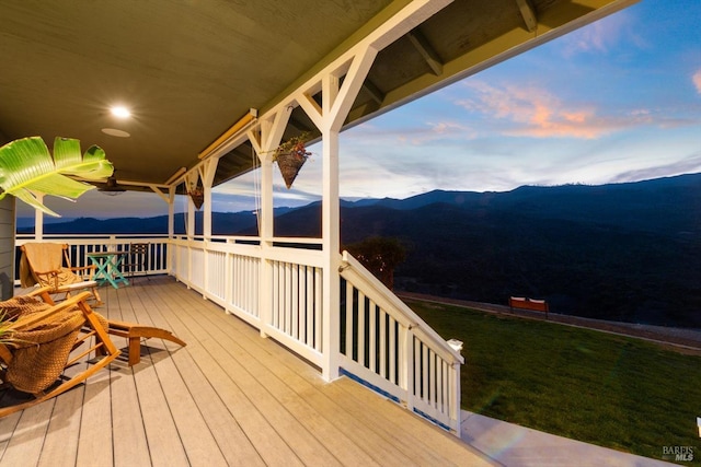 deck at dusk with a mountain view and a yard