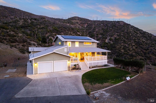 view of front facade featuring solar panels, covered porch, a mountain view, driveway, and stairs