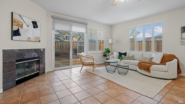 living room featuring a tiled fireplace, light tile patterned flooring, and ceiling fan