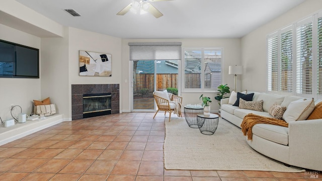 living area featuring visible vents, light tile patterned floors, baseboards, a tiled fireplace, and ceiling fan