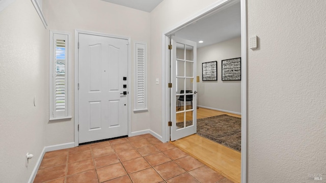 entrance foyer featuring baseboards, light tile patterned flooring, and french doors