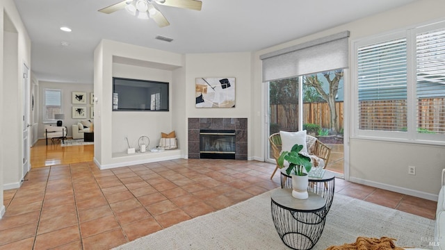 living room with plenty of natural light, a tiled fireplace, ceiling fan, and light tile patterned flooring