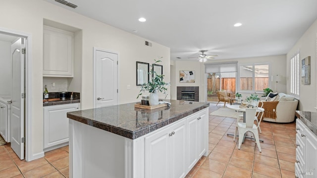 kitchen featuring light tile patterned flooring, a kitchen island, a fireplace, white cabinets, and ceiling fan