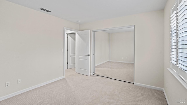 unfurnished bedroom featuring baseboards, visible vents, a closet, and light colored carpet