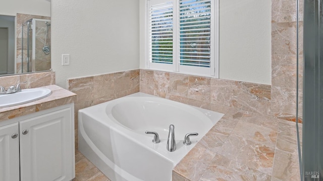 bathroom with a bath, vanity, a stall shower, and a textured wall
