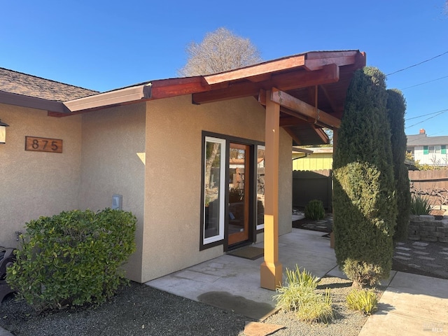 property entrance featuring a patio area, fence, and stucco siding