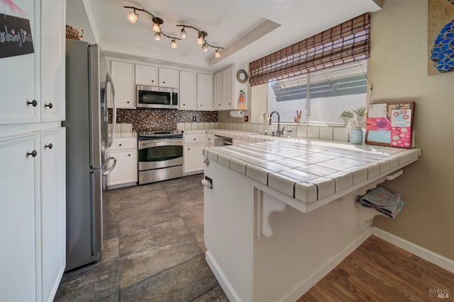 kitchen featuring sink, white cabinetry, appliances with stainless steel finishes, tile counters, and kitchen peninsula