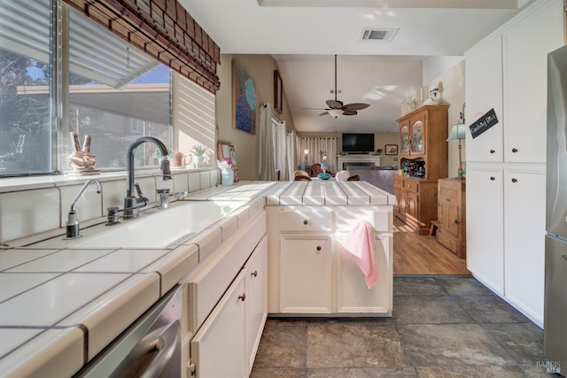 kitchen with ceiling fan, tile countertops, sink, and white cabinets