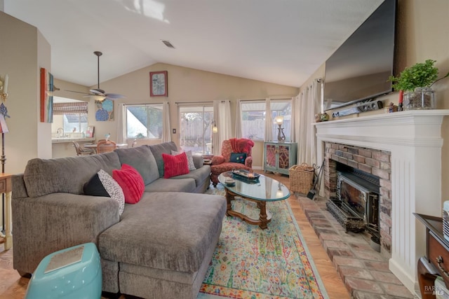 living room with ceiling fan, lofted ceiling, a brick fireplace, and light wood-type flooring