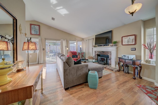 living room with vaulted ceiling, a brick fireplace, and light wood-type flooring