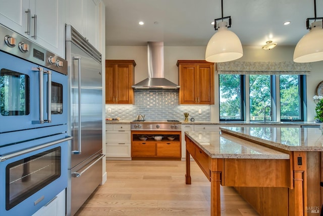 kitchen with white cabinets, hanging light fixtures, stainless steel appliances, and wall chimney range hood