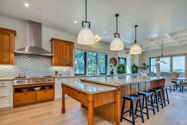 kitchen with hanging light fixtures, a breakfast bar, backsplash, coffered ceiling, and wall chimney exhaust hood