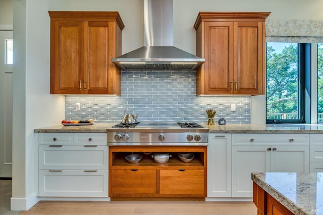 kitchen featuring light stone countertops, wall chimney range hood, white cabinets, stainless steel gas cooktop, and decorative backsplash