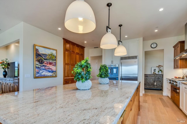 kitchen featuring stainless steel appliances, light stone counters, white cabinets, decorative light fixtures, and light wood-type flooring