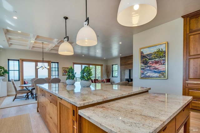 kitchen with light stone countertops, light hardwood / wood-style floors, pendant lighting, coffered ceiling, and a kitchen island