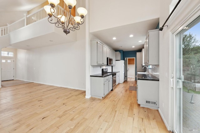 kitchen featuring stainless steel appliances, light hardwood / wood-style floors, hanging light fixtures, and a high ceiling