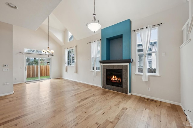 unfurnished living room featuring a notable chandelier, high vaulted ceiling, a fireplace, and light hardwood / wood-style floors