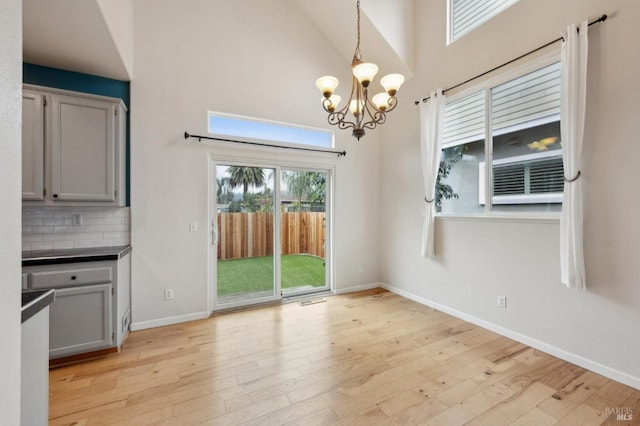 unfurnished dining area featuring an inviting chandelier, high vaulted ceiling, and light hardwood / wood-style flooring