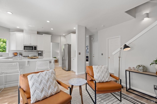 kitchen with appliances with stainless steel finishes, backsplash, white cabinets, kitchen peninsula, and light wood-type flooring