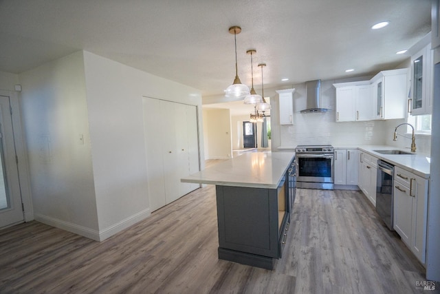 kitchen featuring stainless steel appliances, white cabinets, a kitchen island, decorative light fixtures, and wall chimney exhaust hood