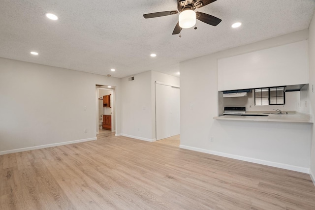 unfurnished living room featuring baseboards, a ceiling fan, light wood-style floors, and a textured ceiling