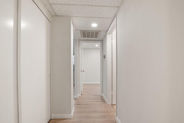 corridor with a paneled ceiling, light wood finished floors, baseboards, and visible vents