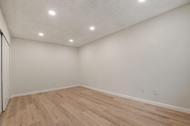 empty room with light wood-style flooring, recessed lighting, baseboards, and a textured ceiling